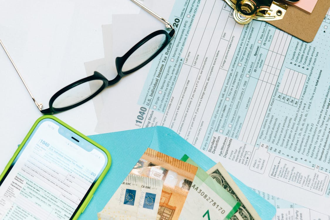 A form, money, a cellphone, and eyeglasses arranged on a table